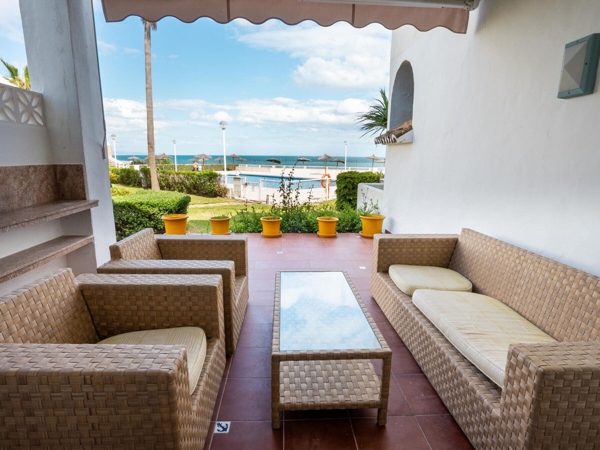 A patio with wicker furniture, a glass table, and a view of the sea.