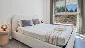 A bedroom with a large bed, a bedside table, a lamp, and a window with a view of trees. - Modern apartment with terrace - ? guests (Mijas)