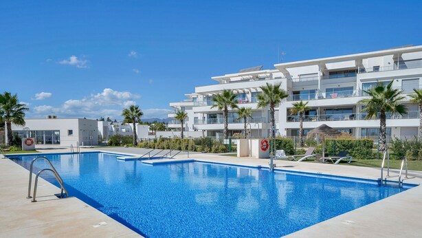 A swimming pool with a lifeguard chair and a lifebuoy, surrounded by palm trees and modern buildings. - Modern apartment with terrace - ? guests (Mijas)