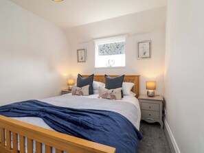A bedroom with a bed, two bedside tables, a window with a view, and wall art. - Lamb Cottage (Billingham)