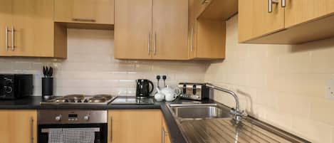 A modern kitchen with wooden cabinets, a stainless steel sink, a black countertop, and a built-in oven.