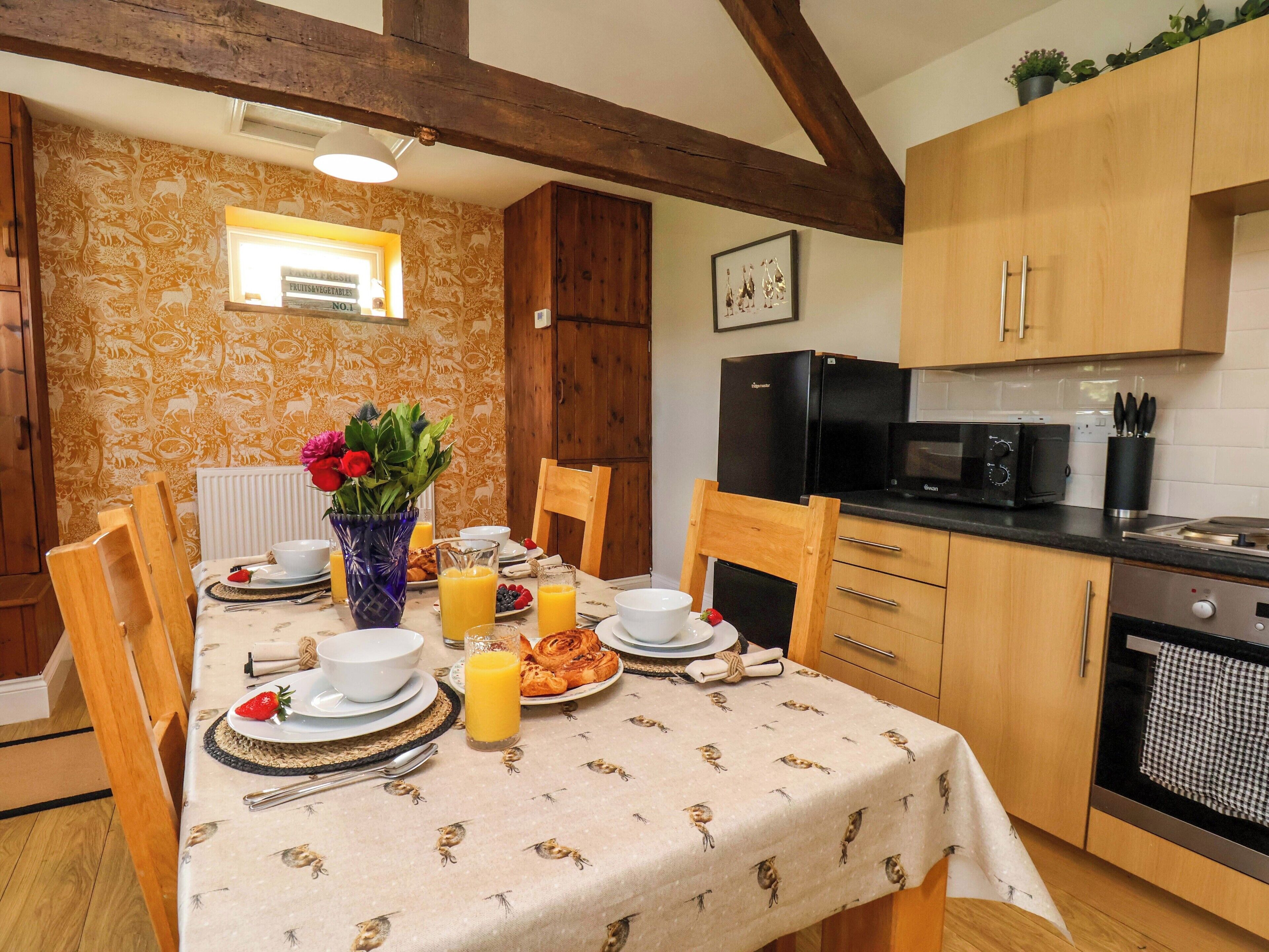 A dining area with a table set for breakfast, a refrigerator, microwave, and a sink in the kitchen.