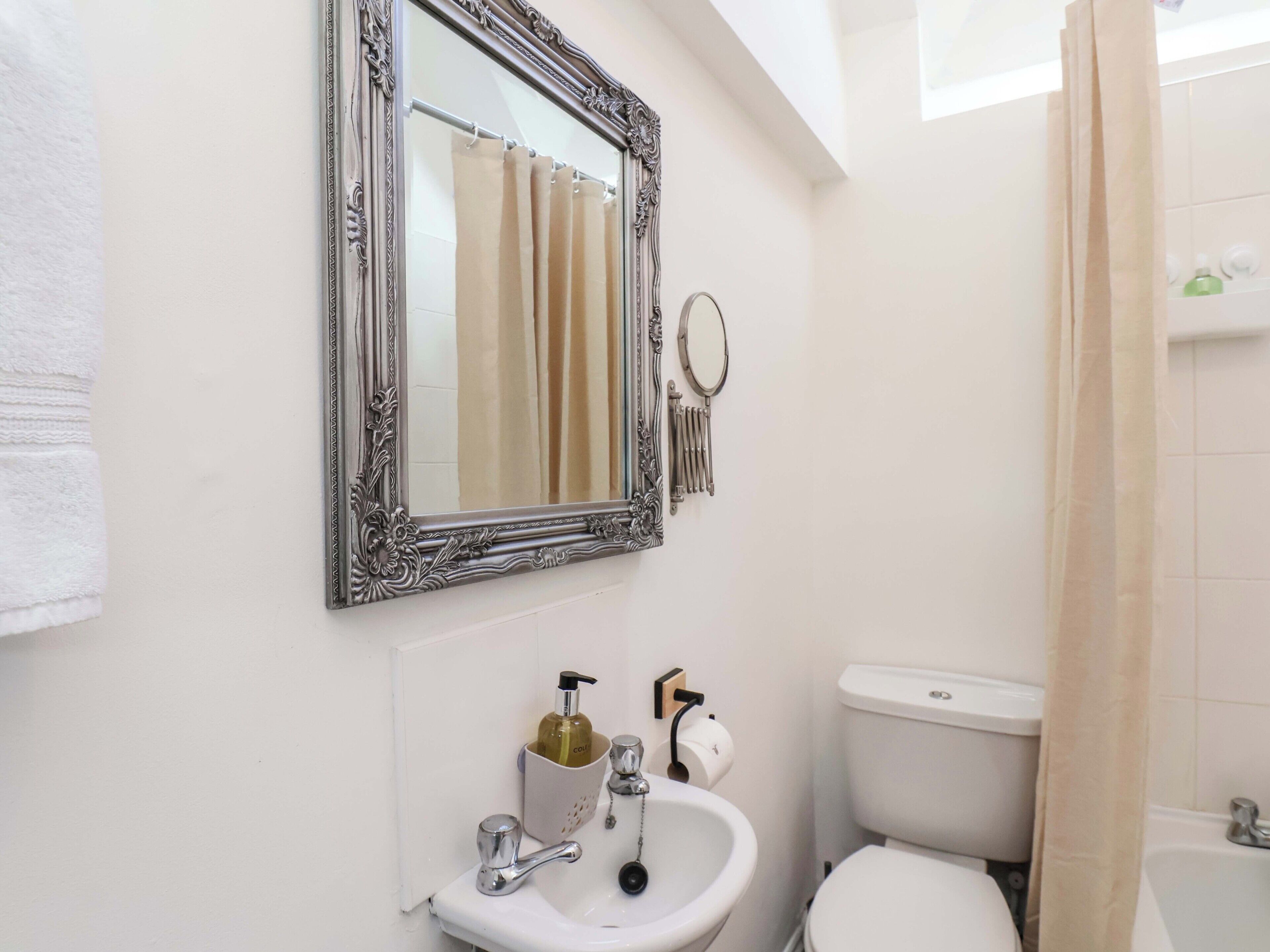 Un baño con un lavamanos blanco, inodoro y espejo con un marco decorativo.