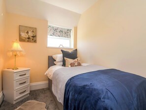 A bedroom with a bed, a nightstand, a lamp, a window with a view, and a wall-mounted painting. - Lamb Cottage (Billingham)