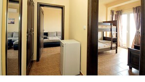A hallway leading to a bedroom with a bunk bed, a small refrigerator, and a window with curtains.
