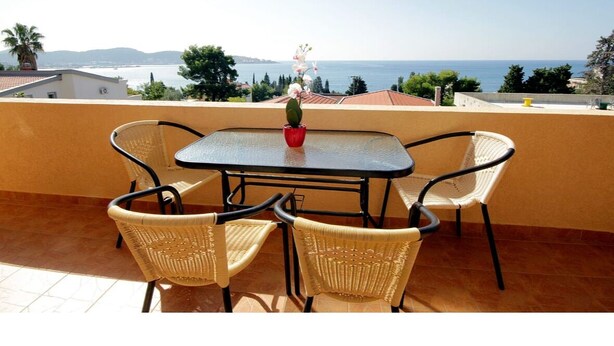 A terrace with a table and chairs, a potted plant, and a view of the sea.