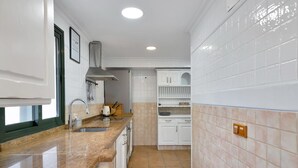 Een keuken met witte kastjes, een granieten aanrechtblad, een inbouwoven en een betegelde spatwand.
