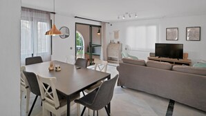 Een moderne woonkamer met een eethoek, een bank, een televisie en een groot raam.