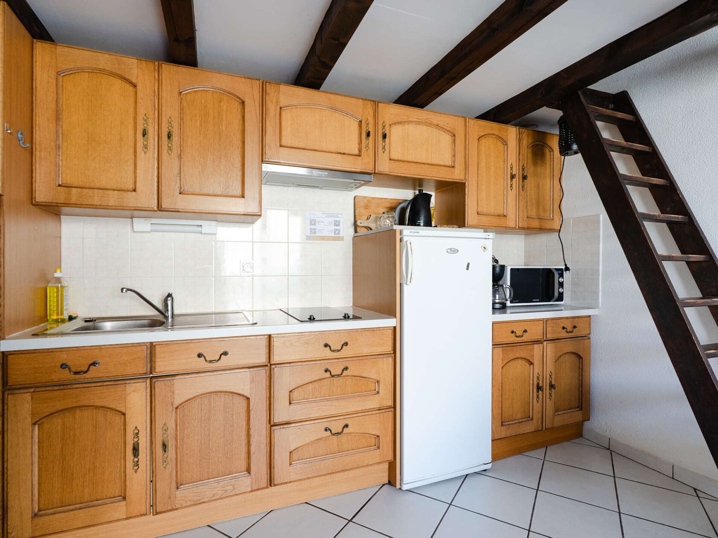 A kitchen with wooden cabinets, a white refrigerator, a microwave, and a stainless steel sink.