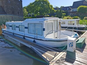 A white boat docked at a pier with a covered deck area, windows, and a name 'ABLETTE' visible.