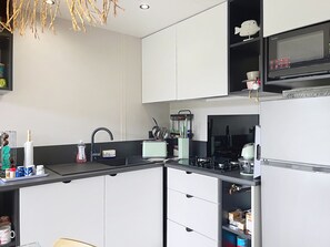 A modern kitchen with white cabinetry, a black countertop, a microwave, and a refrigerator. - Beach house - 6 guests, pool and WiFi (Saint-Pair-sur-Mer)