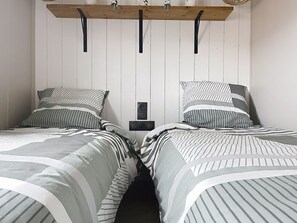 Une chambre avec deux lits, chacun doté de draps à rayures, une étagÚre en bois au-dessus et un haut-parleur fixé au mur.