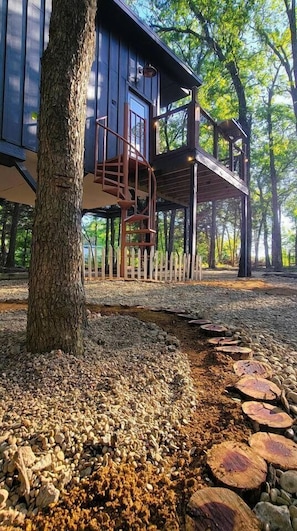A wooden cabin with a spiral staircase, surrounded by trees and a wooden deck.