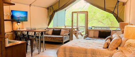 A tented accommodation with a dining area, a bed with patterned bedding, and a television.