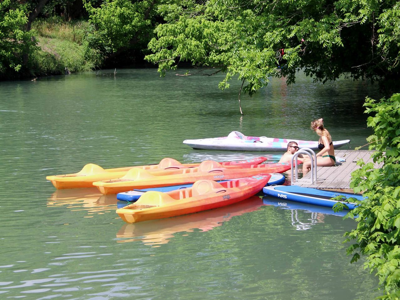 Un río tranquilo con kayaks amarrados a un muelle de madera.