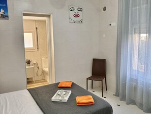 Ein Hotelzimmer mit einem Bett, einem Sessel, einem durchgegangenen Tür erkennbaren Badezimmer und einem Bild an der Wand.