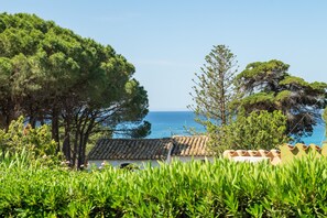 A coastal view with trees, a building with a tiled roof, and the sea in the background. - Bigflower’s House Sardinia: Sea View, Pool & Air Conditioning (Campulongu)