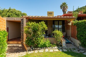 A house with a stone entrance, a covered porch, and a small garden with a palm tree. - Bigflower’s House Sardinia: Sea View, Pool & Air Conditioning (Campulongu)