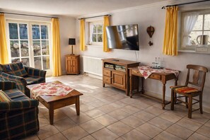 A living room with a sofa, a coffee table, a TV, a small cabinet, and a chair. - Charming Apartments in a Half-Timbered House (Egestorf)