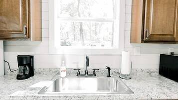A kitchen with wooden cabinets, a stainless steel sink, a coffee maker, and a window with a view of trees.