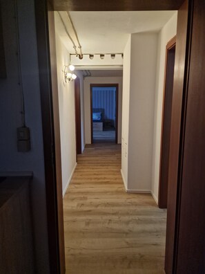 A hallway with wooden flooring leading to a bedroom with a bed and a nightstand.