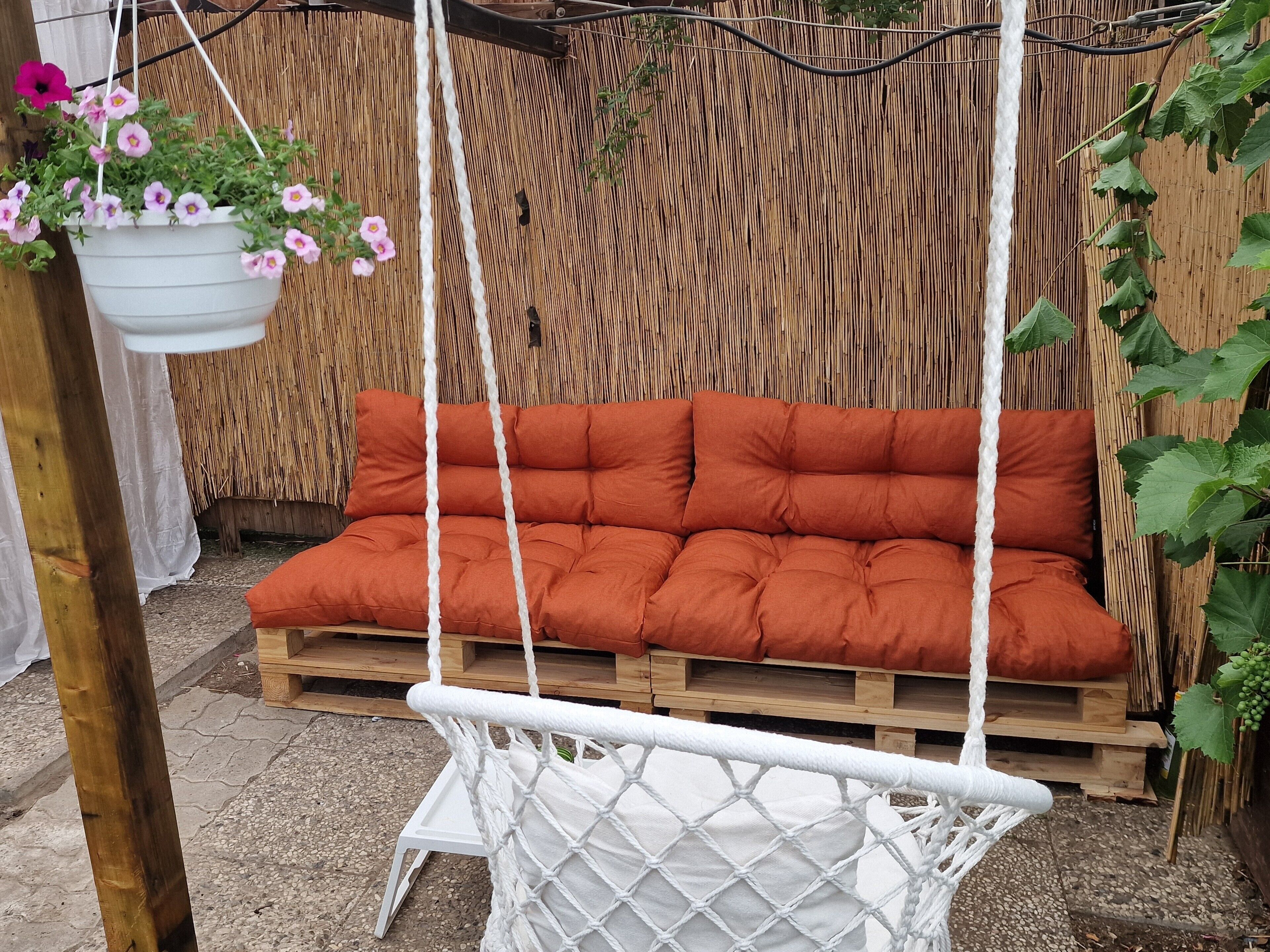 A hanging chair with a white net and a cushioned orange seat, suspended by ropes.