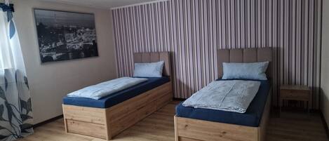 A room with two wooden beds, a striped curtain, a ceiling fan, and a cityscape painting.