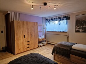 A room with a wooden wardrobe, a radiator, a window with curtains, and a bed. - Vacation Room with Private Kitchen, Bathroom, and Washing Machine (Sibbesse)