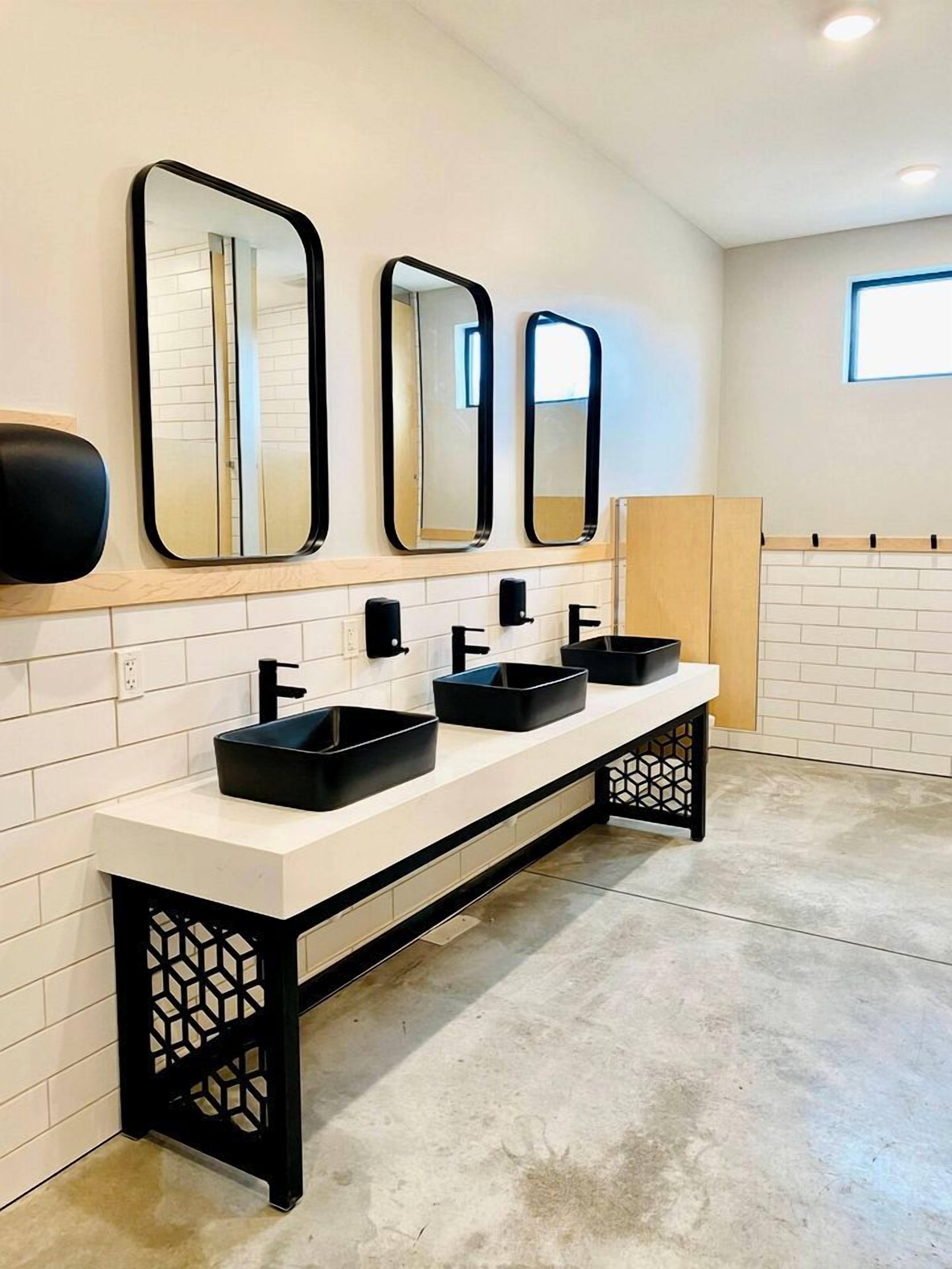 A modern bathroom with three sinks, black soap dispensers, and three wall mirrors.