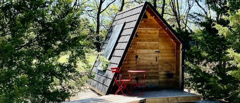 Una cabaña de madera con techo inclinado, un pequeño porche y una mesa con sillas.