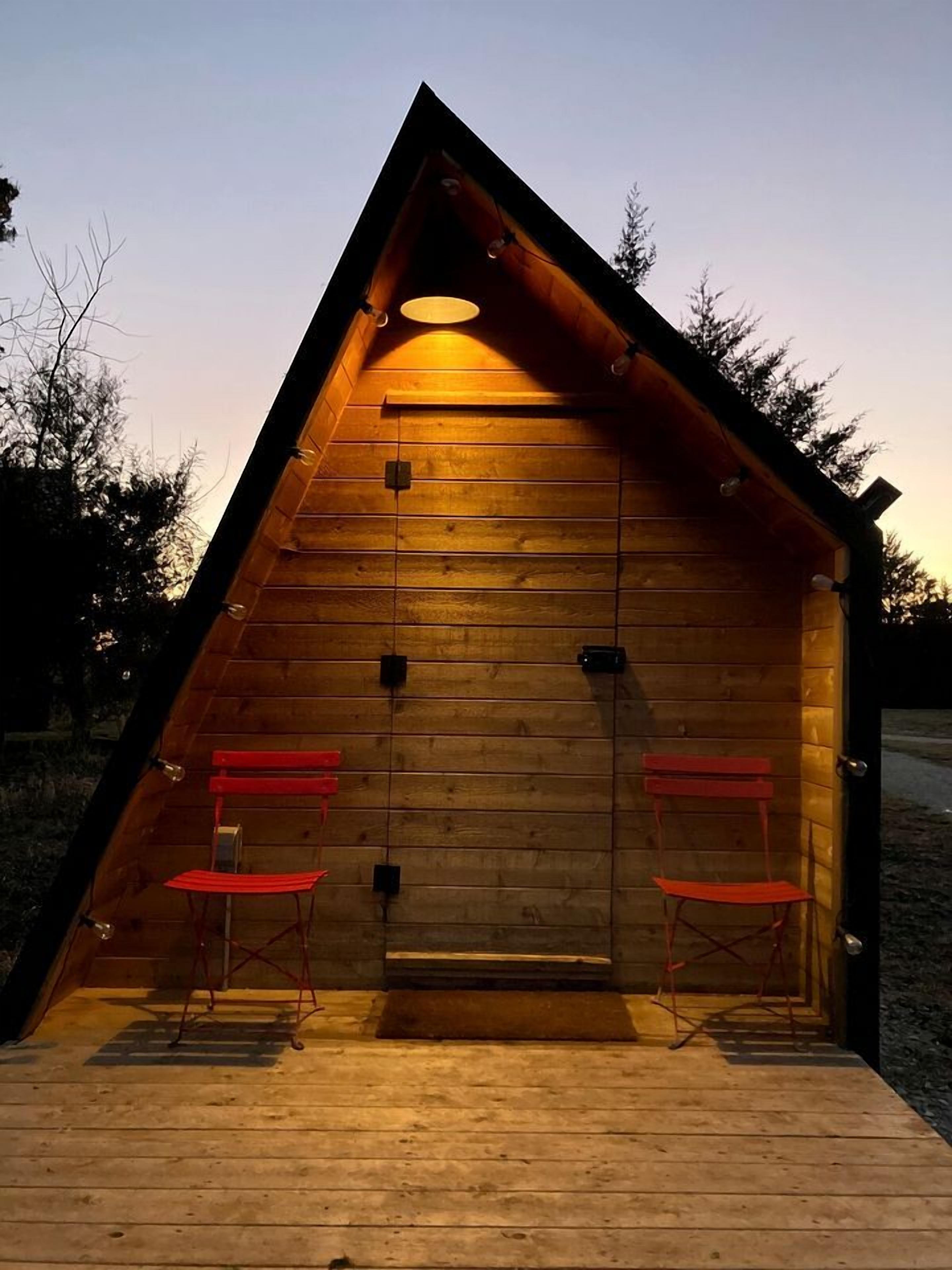 A wooden cabin with a sloped roof, two red chairs, and a single light fixture.