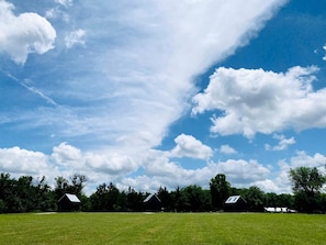A rural landscape with a clear sky, green field, and several buildings with sloped roofs.