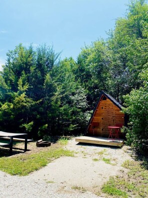 A small wooden cabin with a sloped roof, surrounded by dense trees.