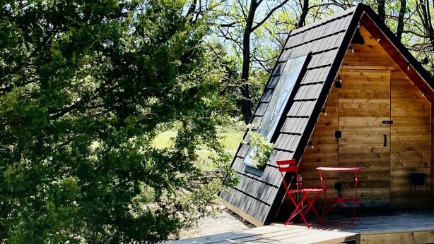 A wooden cabin with a sloped roof, a small porch, and a table with chairs. - Charming A-Frame Cabin Experience with Campfire Vibes in Humboldt, Kansas (Humboldt)