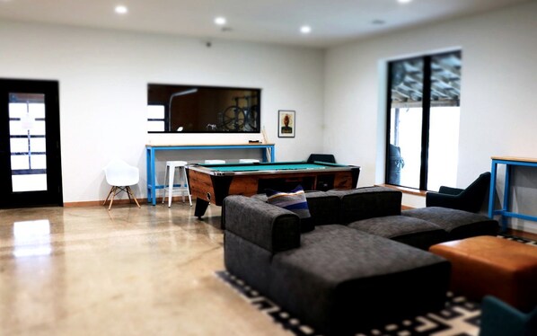 A modern living room with a pool table, comfortable seating, and a large window.