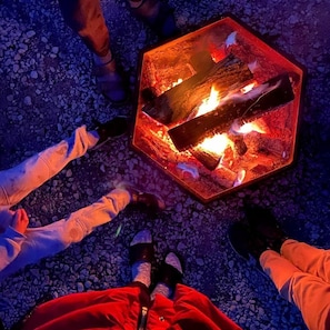 Un grupo de personas sentadas alrededor de un pozo de fuego sobre terreno rocoso.