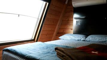A bedroom with a bed, pillows, a blanket, a window, and an air conditioning unit.