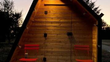 Une cabane en bois avec un toit en pente, deux chaises rouges et un seul luminaire.