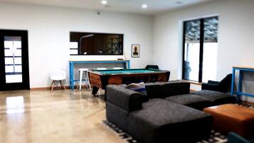 A modern living room with a pool table, comfortable seating, and a large window.