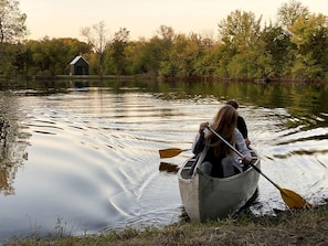 Una persona en una canoa sobre aguas tranquilas, con un edificio pequeño al fondo.