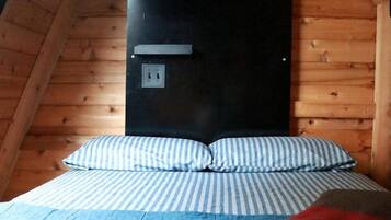 Een slaapkamer met een schuine kap, een bed met gestreepte beddengoed, een zwart hoofdeinde en een wandairconditioner.