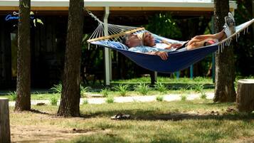 A hammock between trees in a park with a covered area in the background.