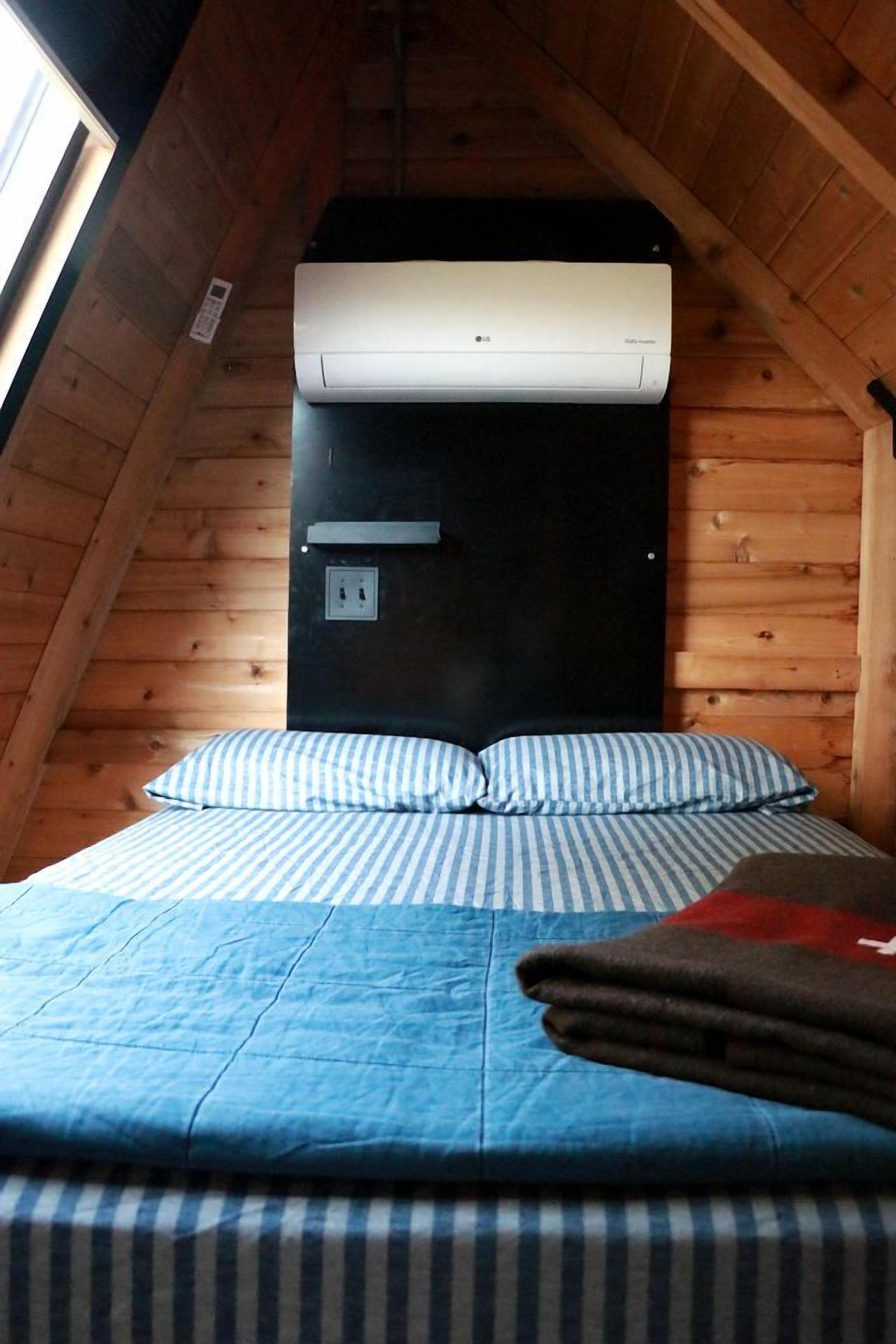 A bedroom with a sloped ceiling, a bed with striped bedding, a black headboard, and a wall-mounted air conditioner.