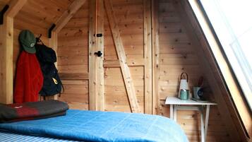 A small attic room with a sloped ceiling, a bed with a blue blanket, a ladder, and a small table with a cup and a mug.