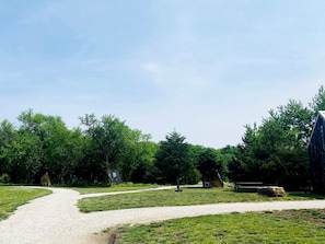 Un sendero de grava que atraviesa un área con césped, árboles y una pequeña construcción.