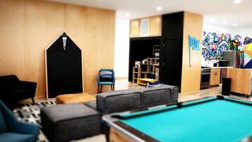 A pool area with a pool table, a blue armchair, a grey sofa, and a small wooden cabinet.