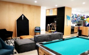 A pool area with a pool table, a blue armchair, a grey sofa, and a small wooden cabinet.