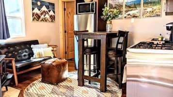 A compact living space with a sofa, a round coffee table, a kitchen area with a stove and microwave, and a dining table with chairs.