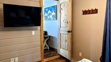 A room with a television mounted on the wall, a wooden door leading to another room, and a coat rack on the wall.