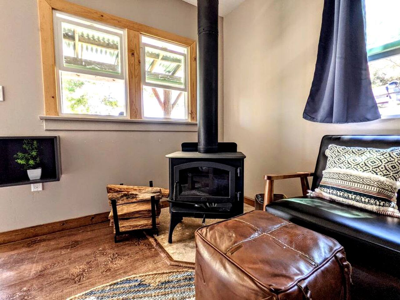 Ein gemütliches Wohnzimmer mit Kaminofen, Fenster mit Aussicht, einer Ledersofa und einem Holzstuhl.